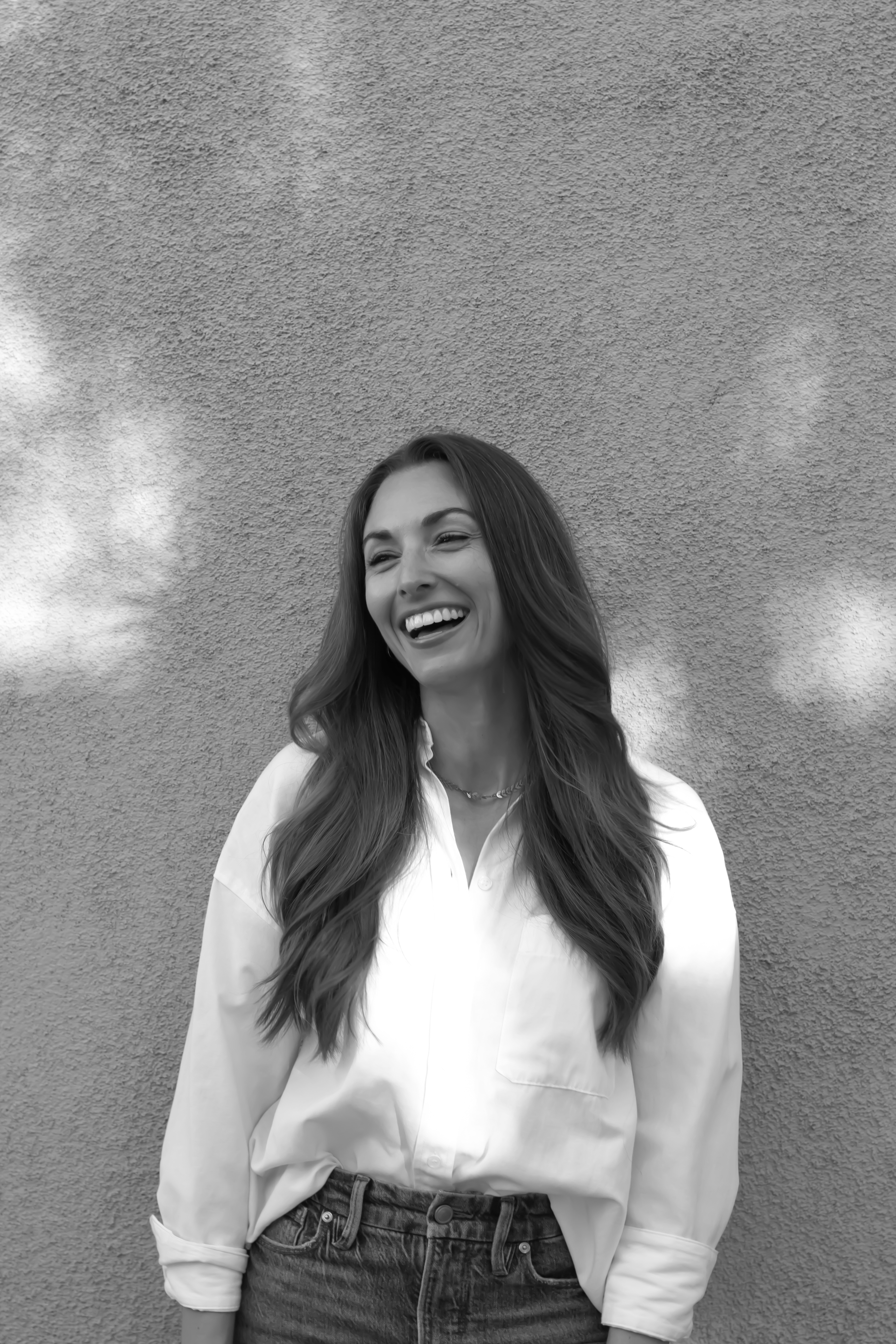 A black and white photo of a girl in a white blouse looking off to the left and laughing