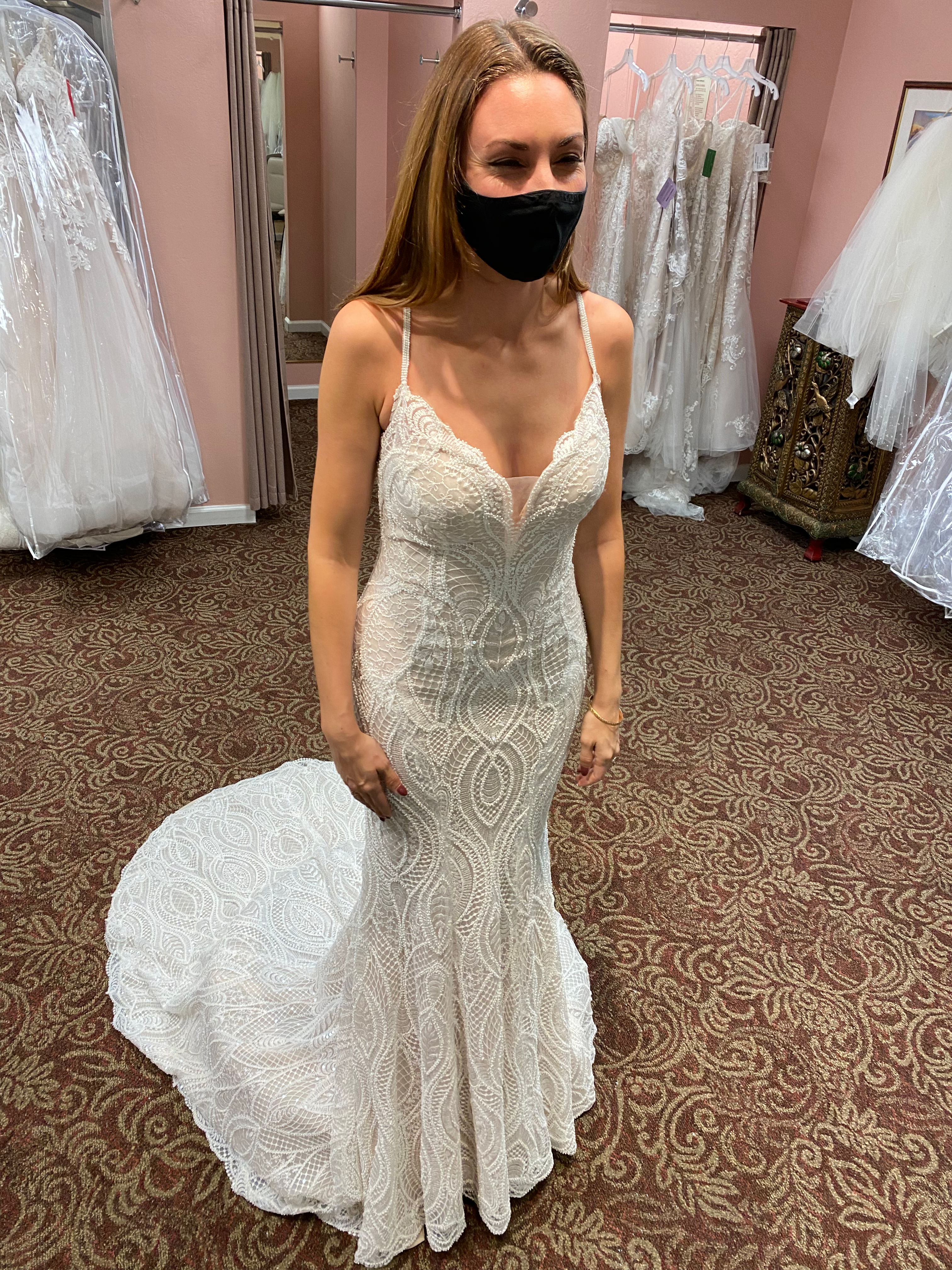 Tara in her wedding dress in a bridal boutique with a mask on looking in a mirror.