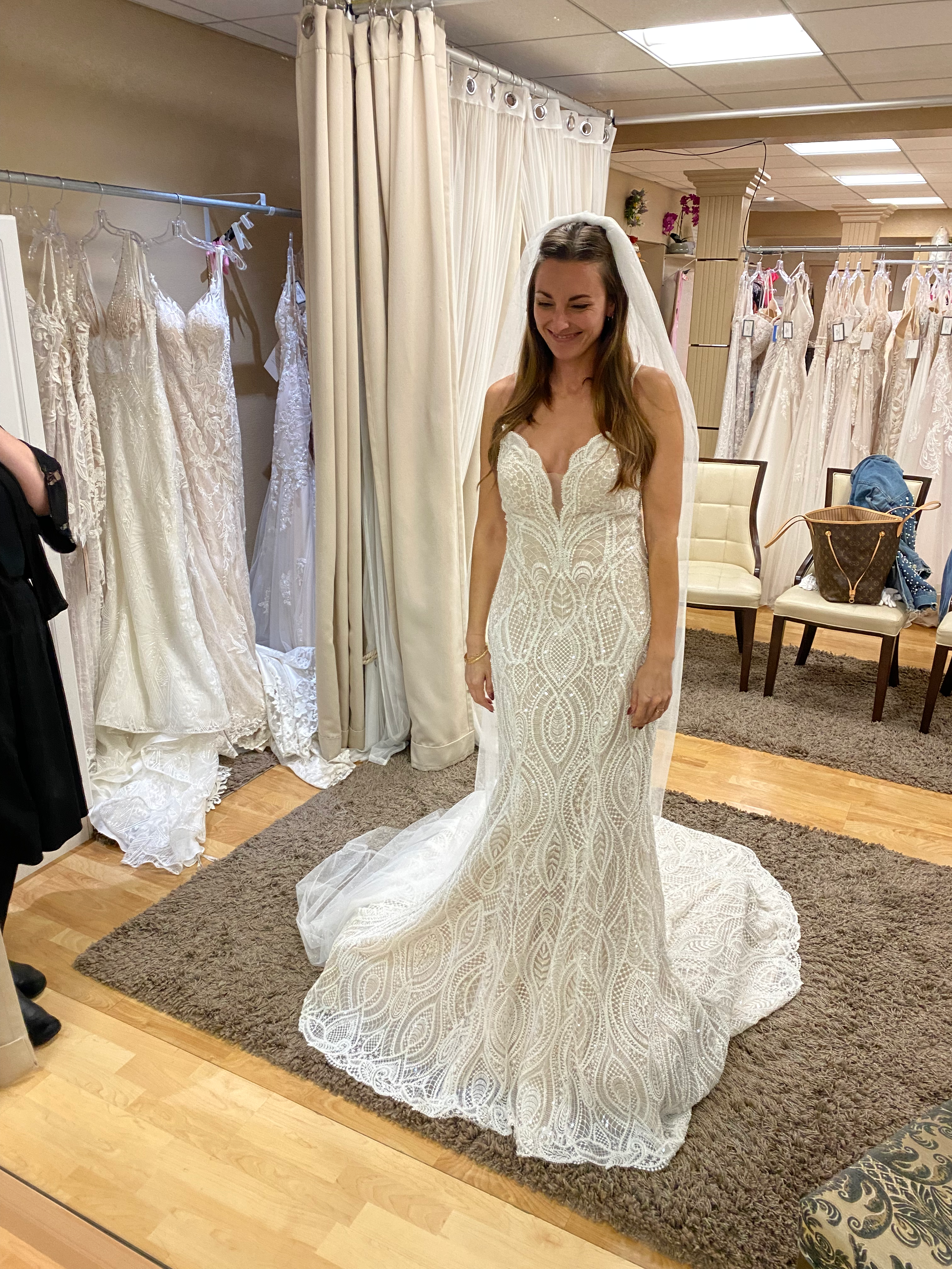 Tara in her wedding dress in a bridal boutique, looking in the mirror and smiling.