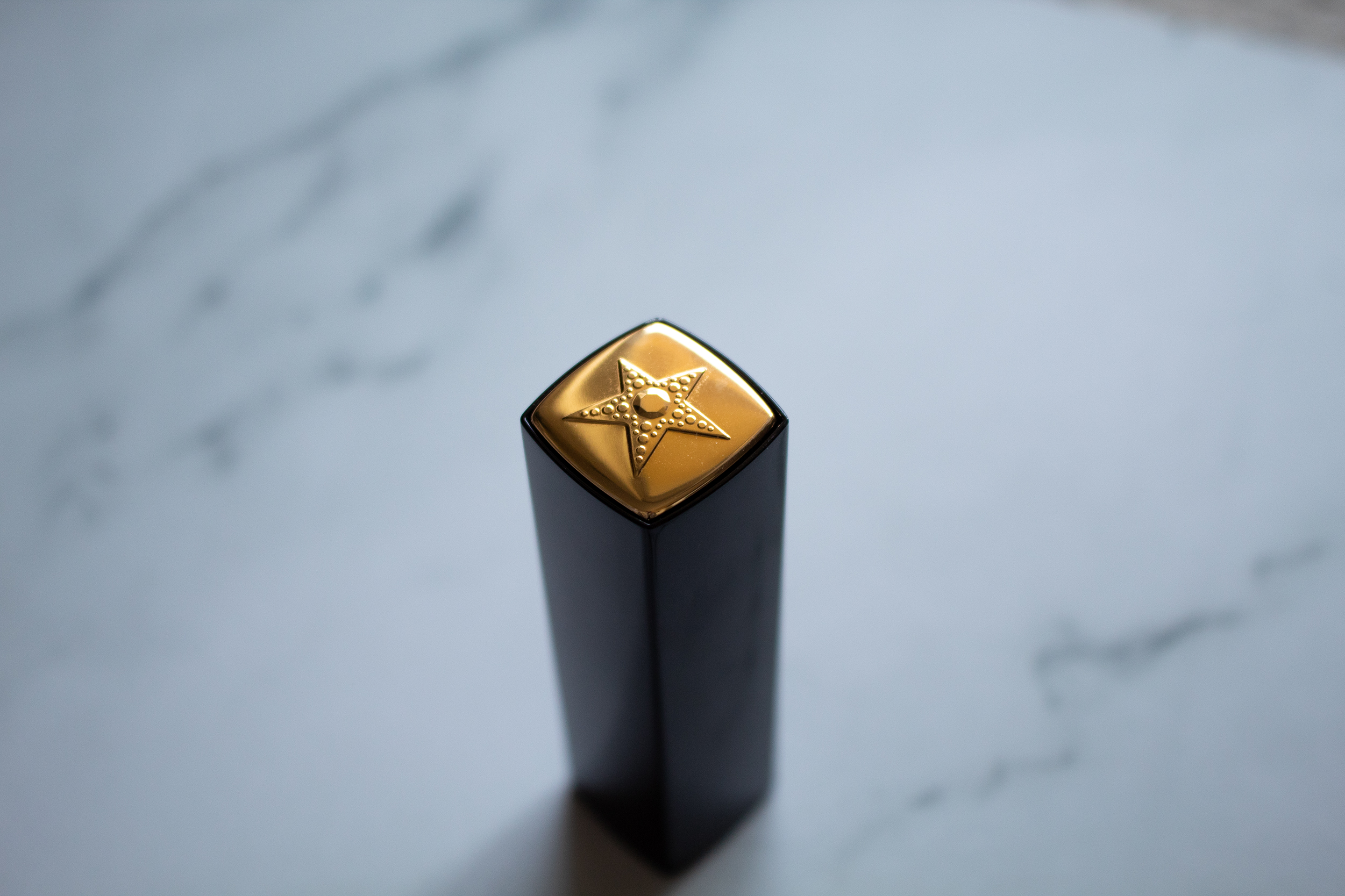 A black lipstick tube with a gold top and a star against a white marble background