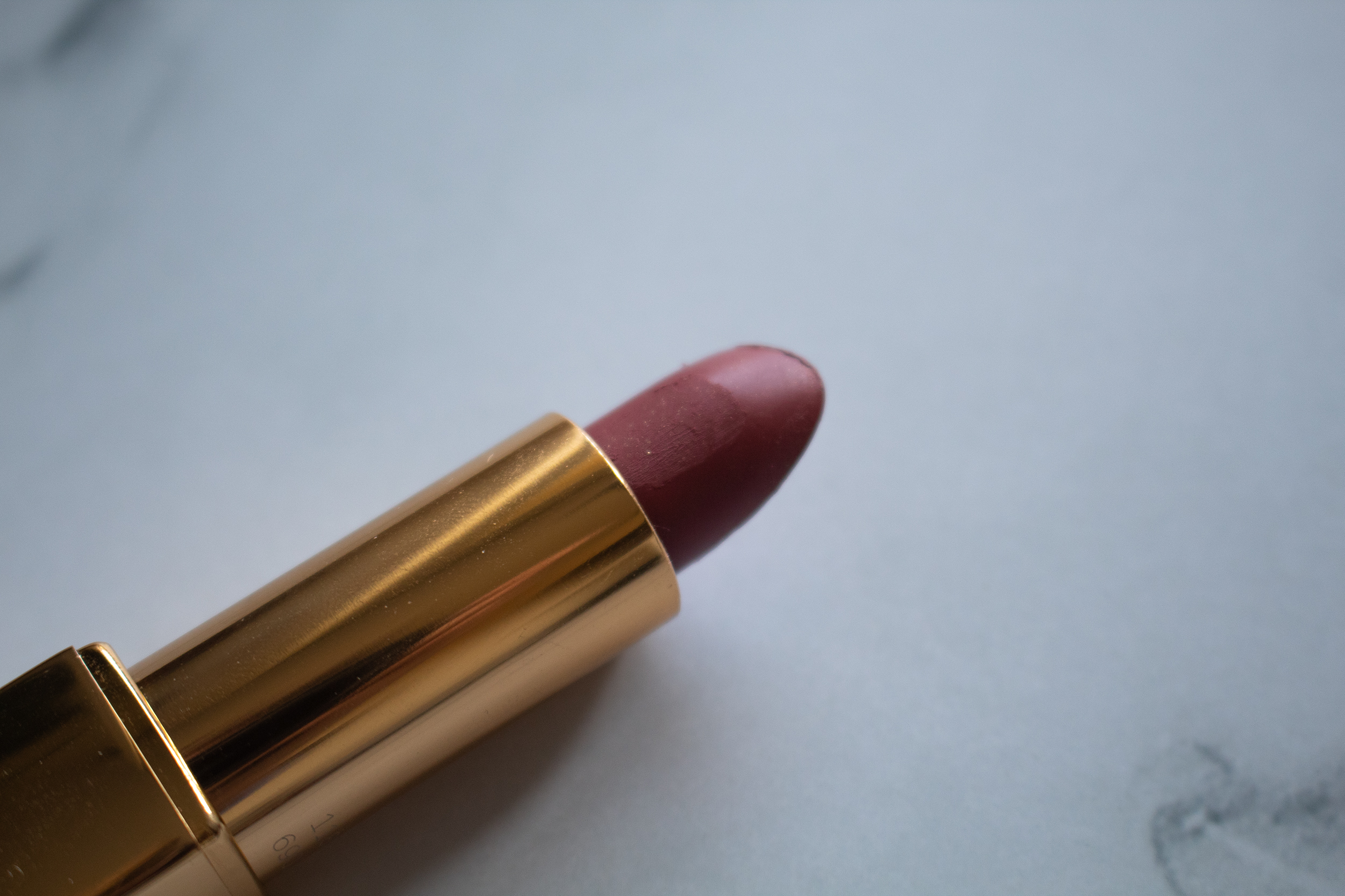 An open gold lipstick with a dark rose pink hue against a white marble background