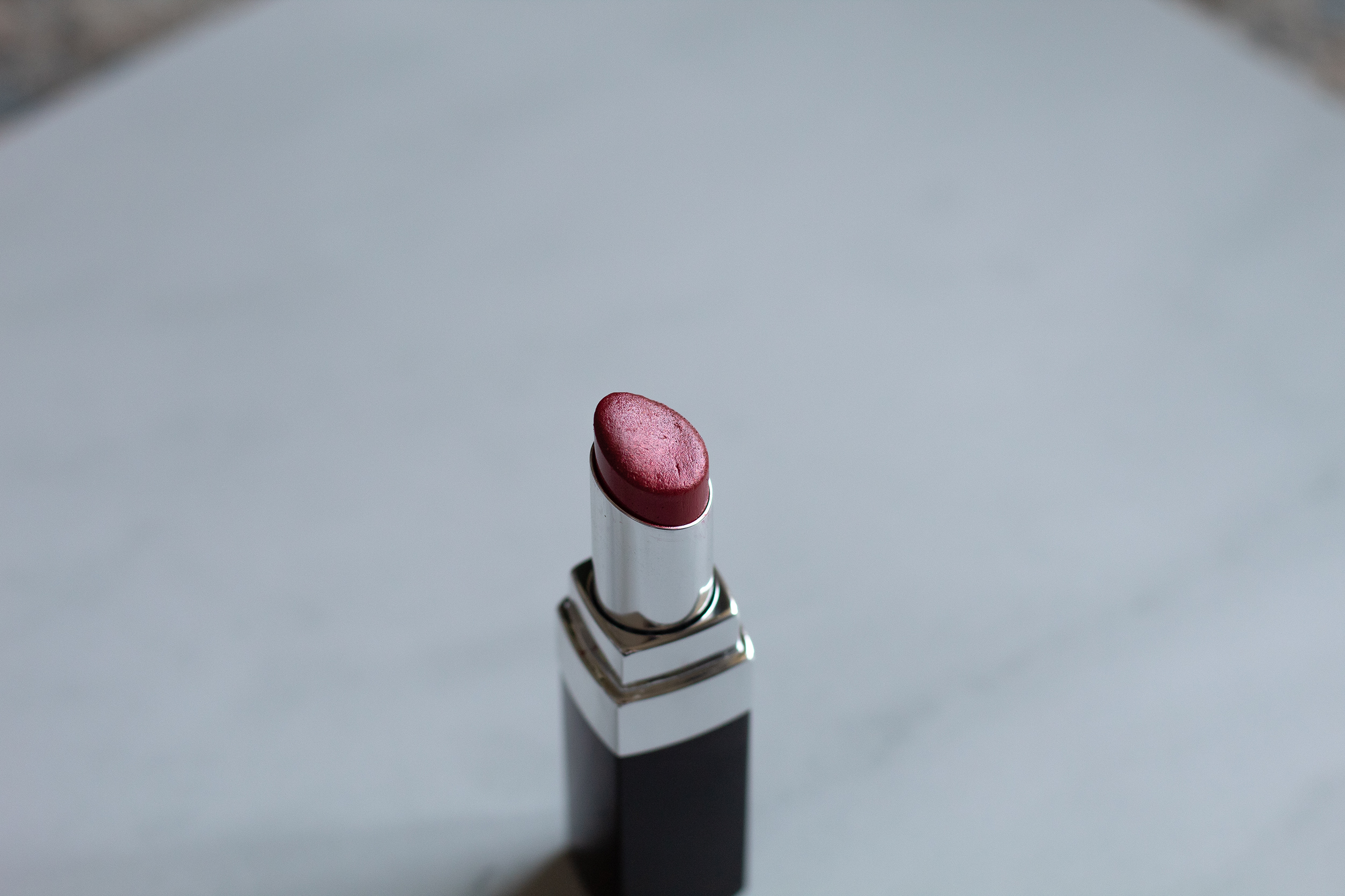 A black and silver lipstick tube that's open to reveal a red lipstick shade against a white marble background