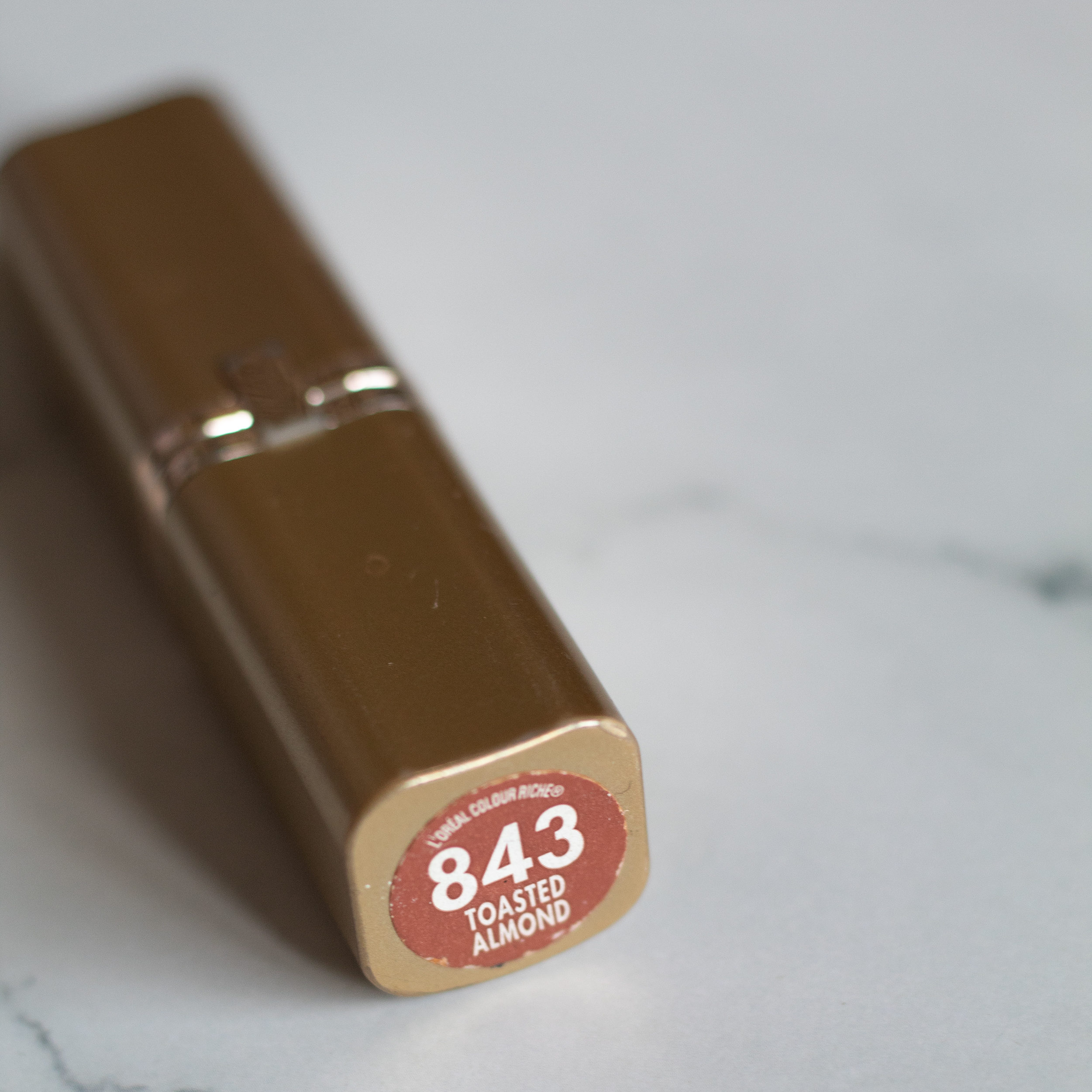 Gold lipstick case with the bottom showing and says 843 Toasted Almond