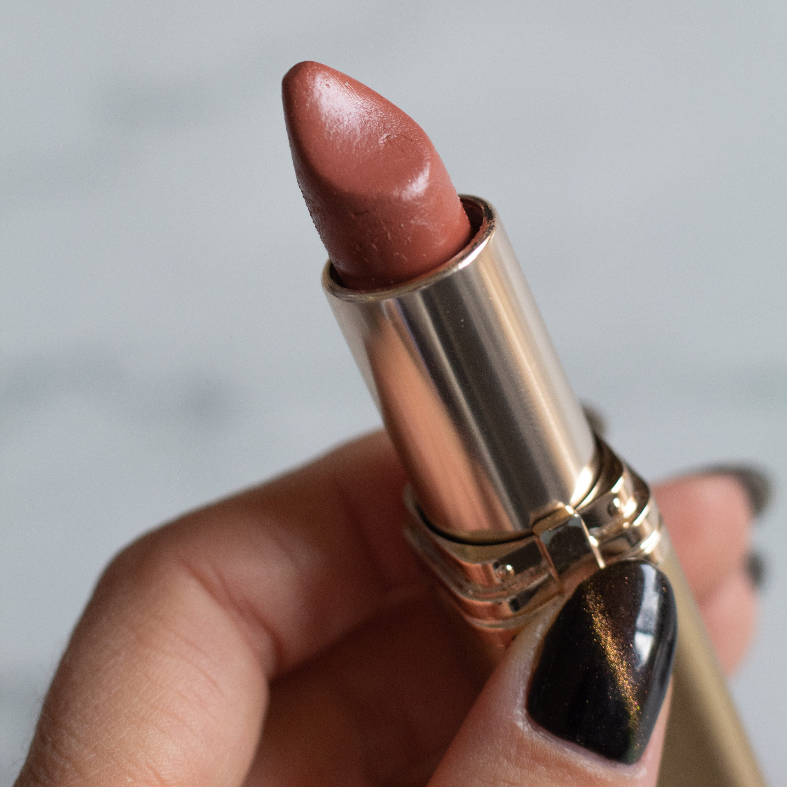 Close up of woman holding a lipstick that's open to show a toasted almond color