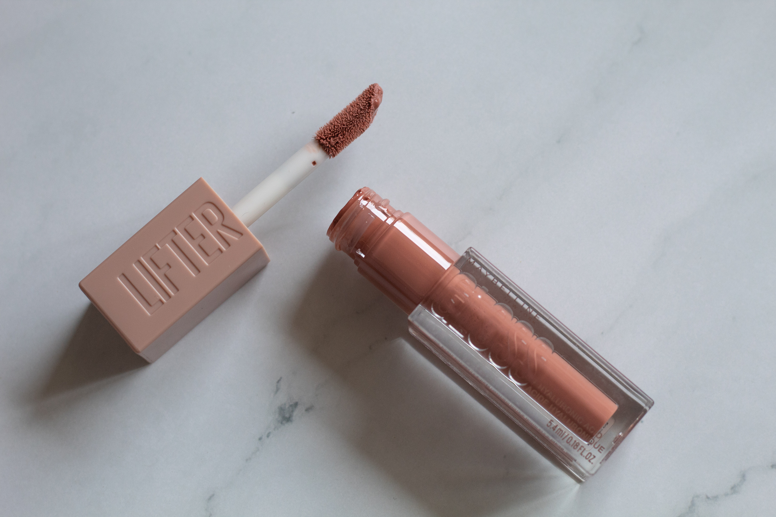 Lifter gloss from Maybelline in a nude brown shade against a white marble background
