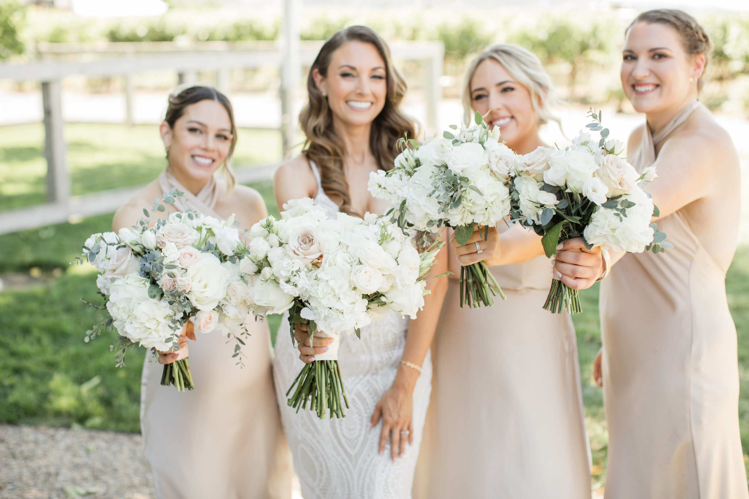 Tara and her bridesmaids in champagne dresses holding out their bouquets and smiling.
