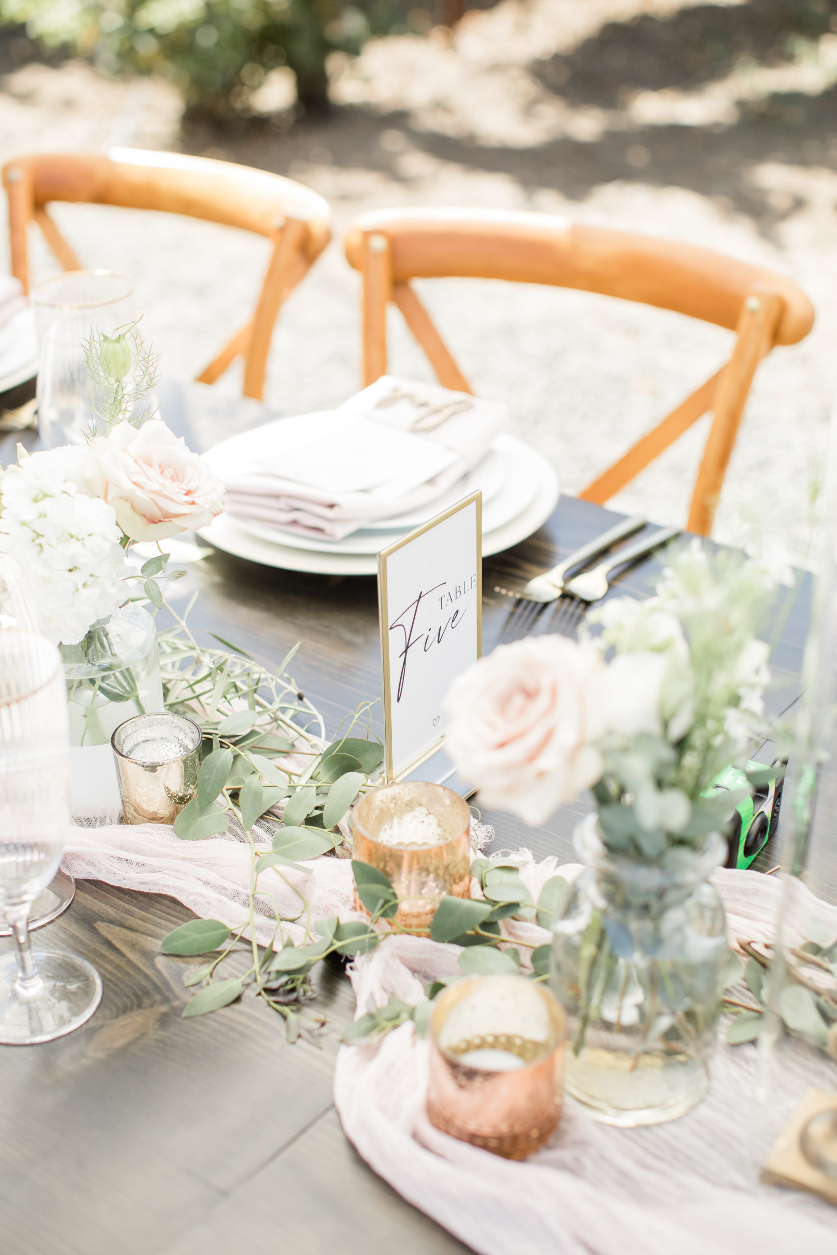 White and blush roses, gold votive candles, and greenery on a wedding dinner table.