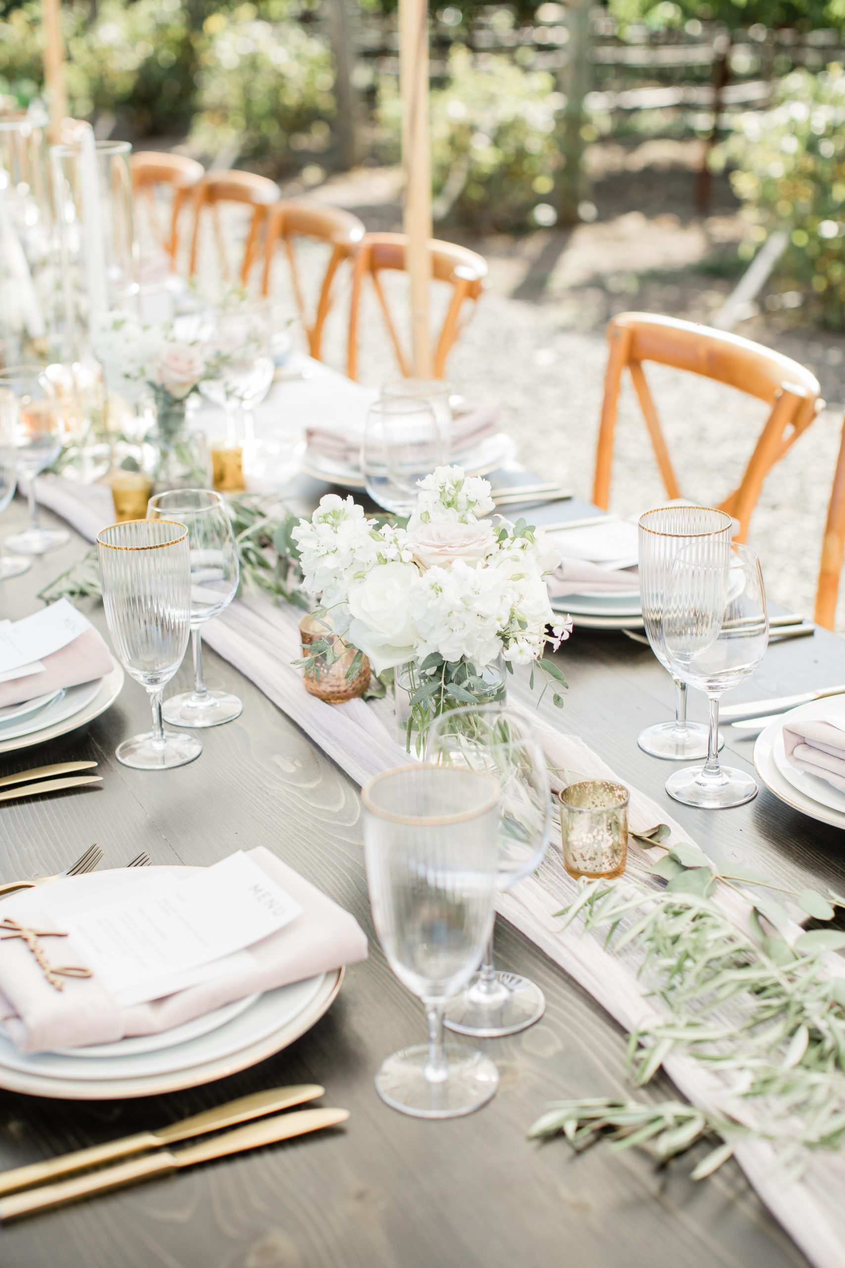 White and blush roses, gold votive candles, and greenery on a wedding dinner table.