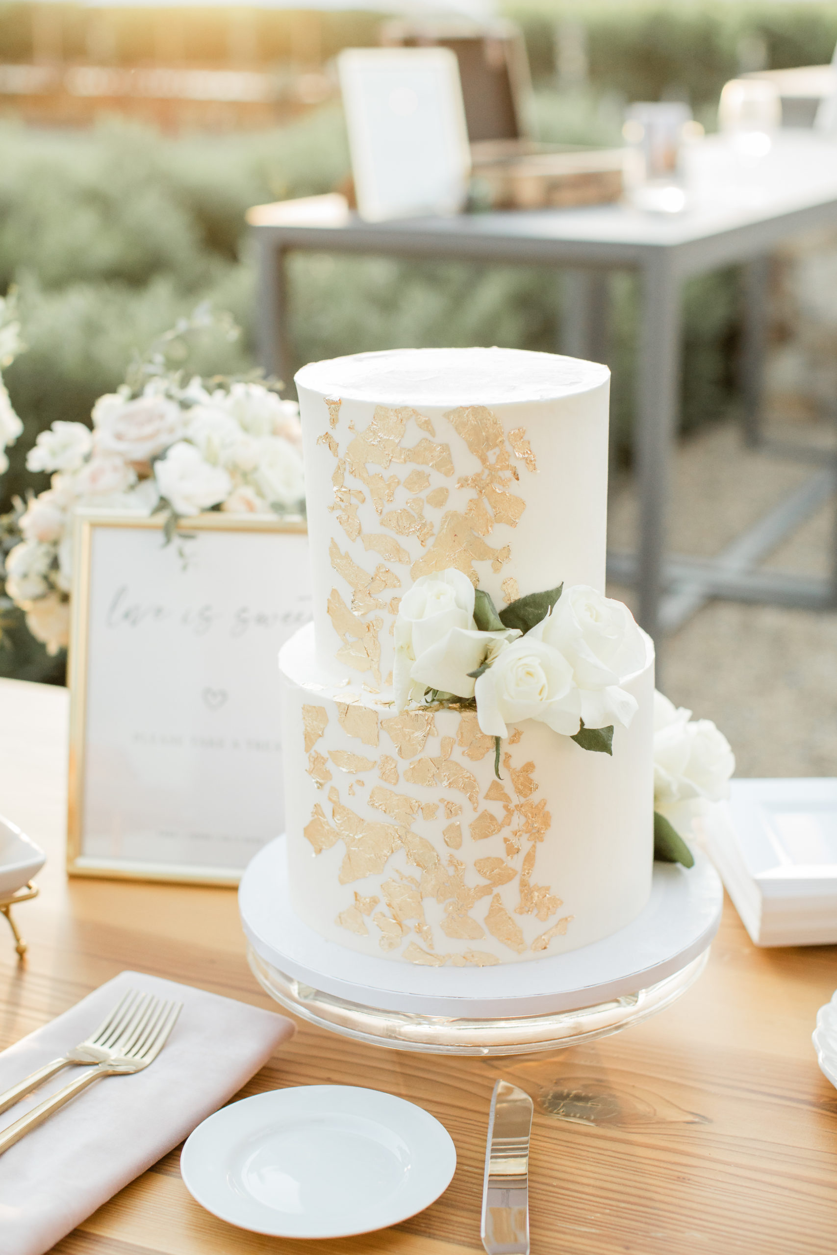 A white wedding cake with gold accents and white roses placed on the side.