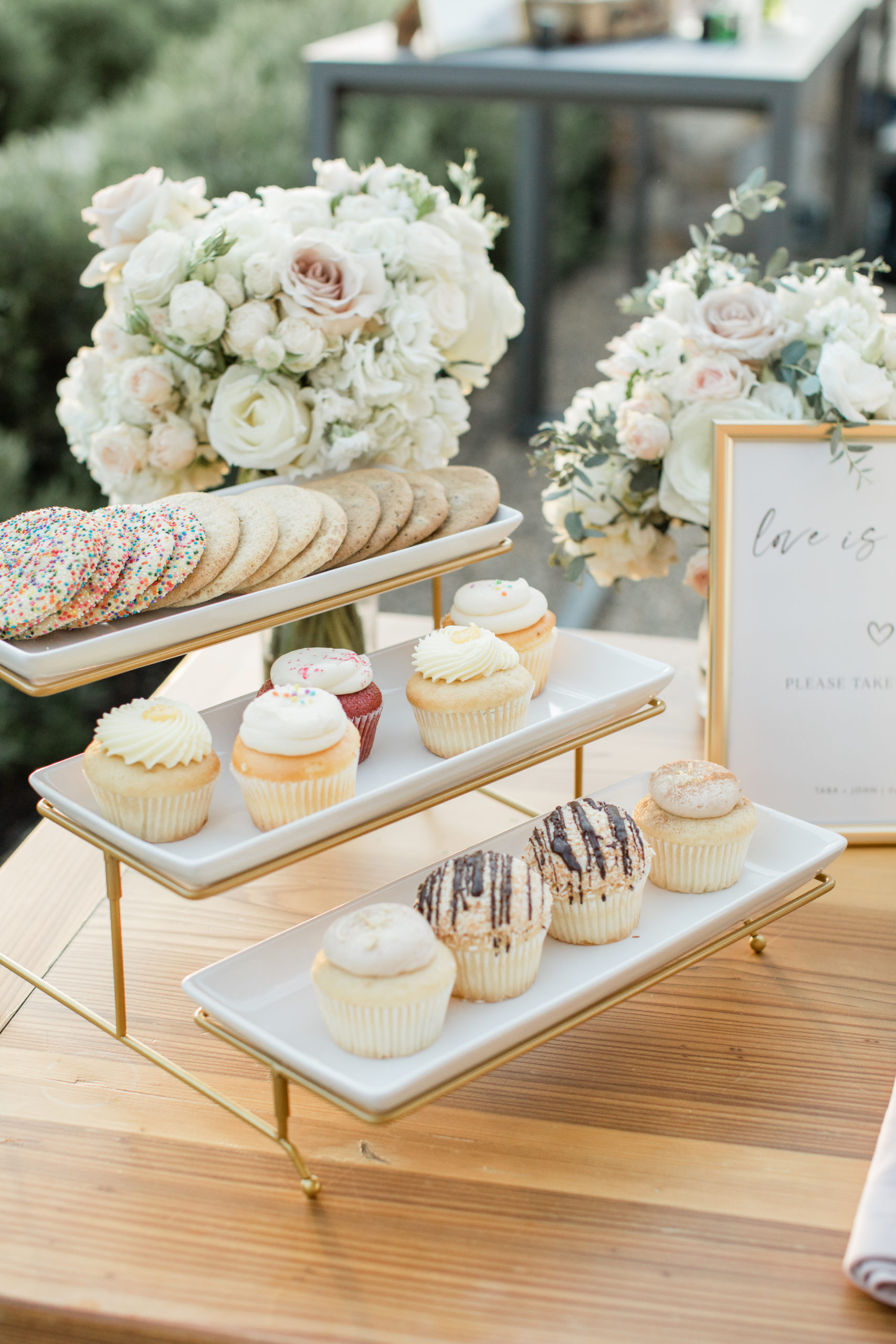 A wedding dessert table with a 3-tier gold dessert tray, holding cookies and cupcakes.