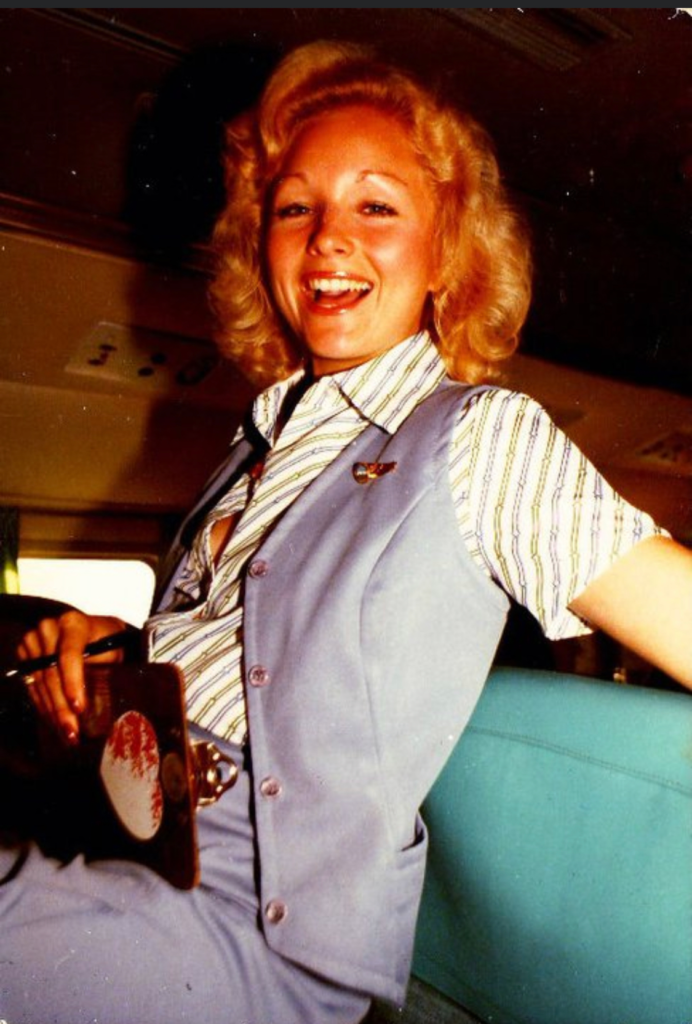 A young blonde flight attendant with short curly hair smiling at the camera
