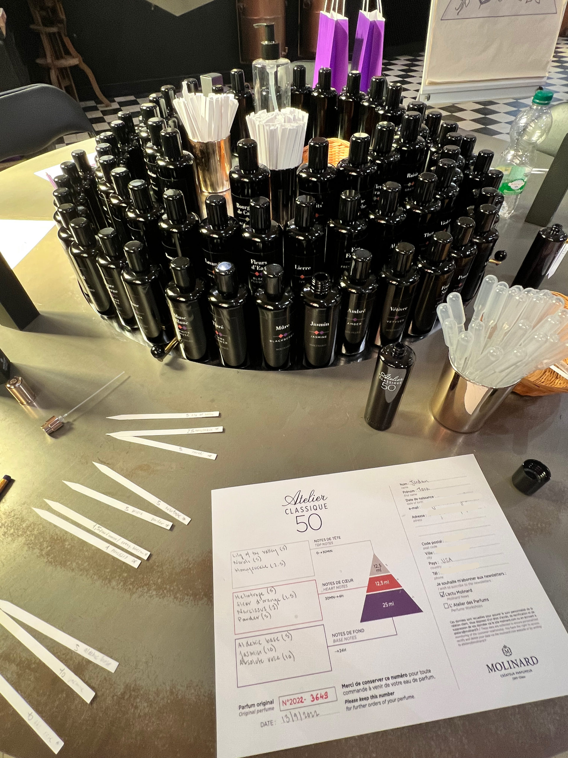 Small black vials of perfume scents in a circle with a white piece of paper and thin white strips of paper on the table below it