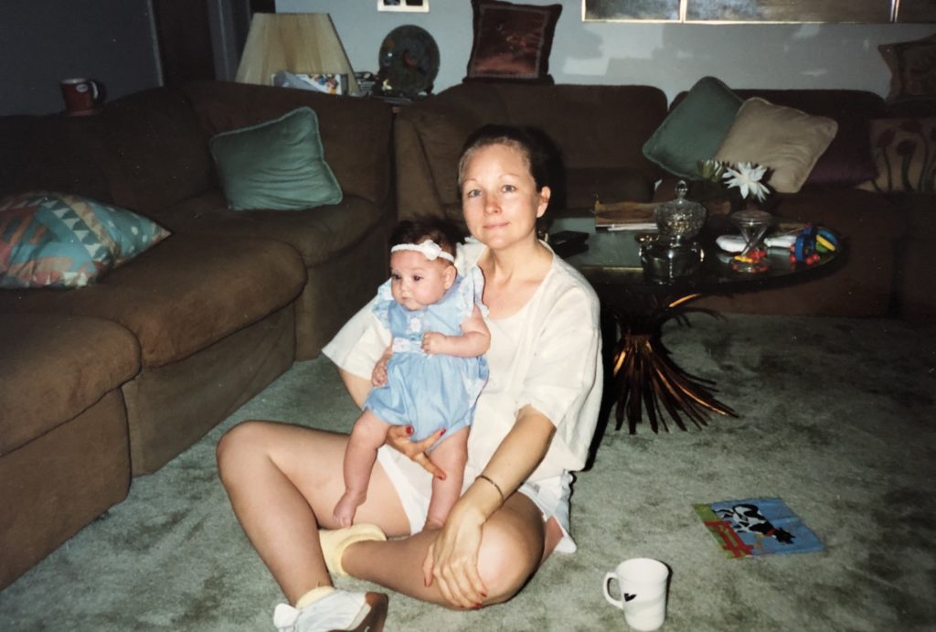 A mother with blonde hair and brown-haired baby girl sitting on the floor