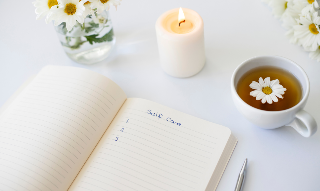 A notebook with "self care" writing, a cup of tea, and candle